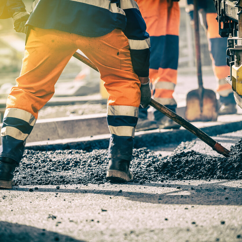 Decorative Image - "Construction workers in high-visibility clothing using shovels to spread asphalt on a road during a paving project."