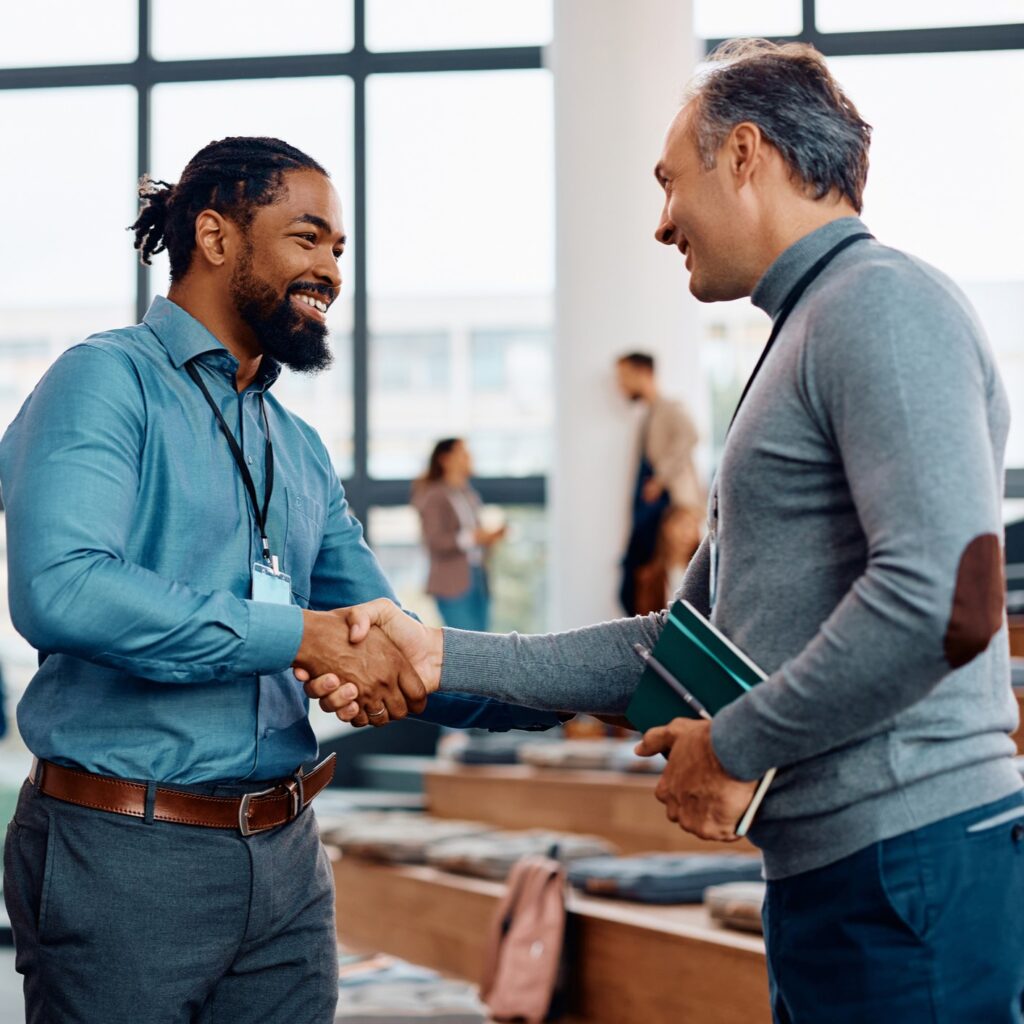 Decorative Image - "Two men in professional attire shaking hands in a modern office or conference setting, engaging in a business or networking conversation."