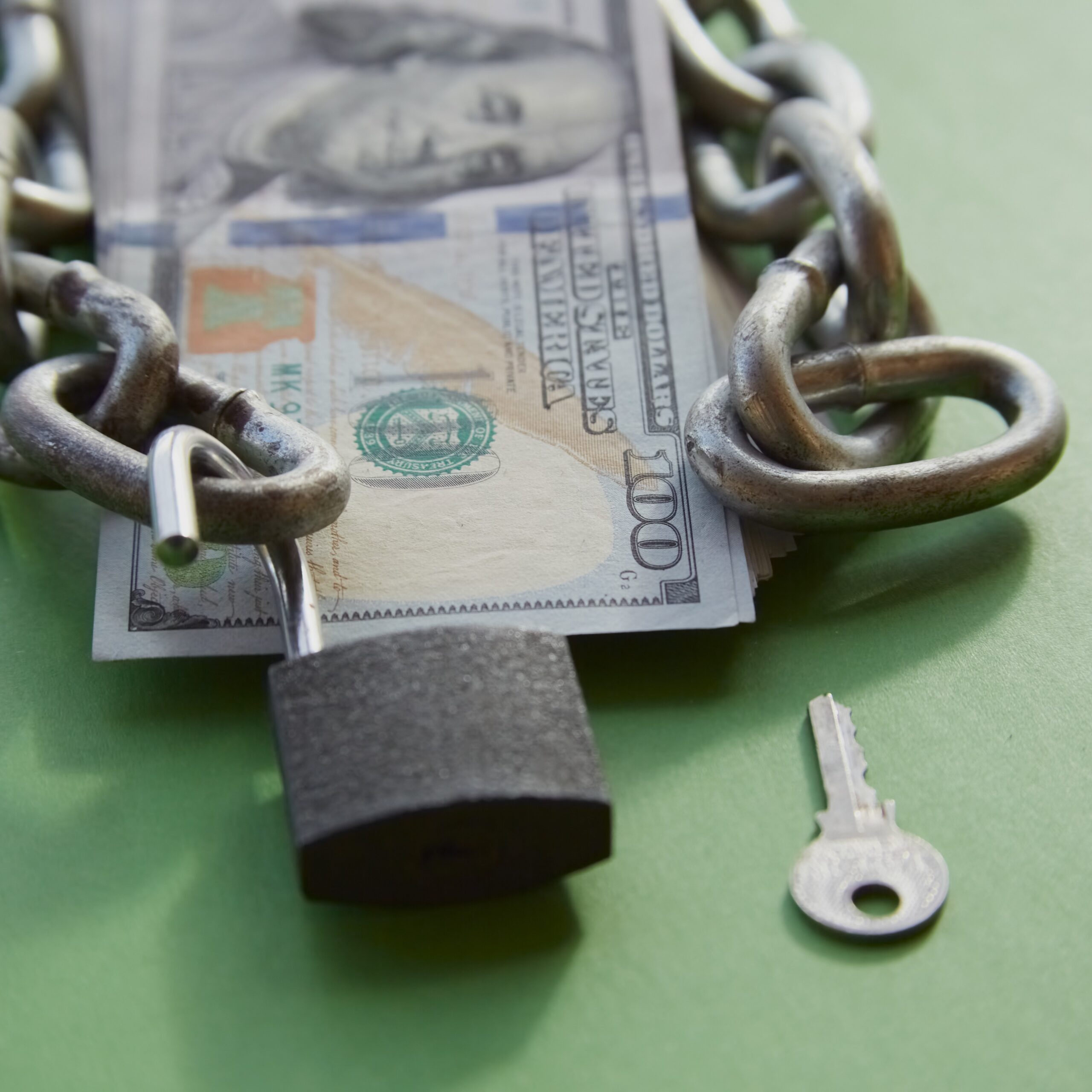 Decorative Image - "Hundred-dollar bills with a chain on them and an open lock and key nearby on green cloth, unlocking funds, unlocked money, unlocking an account"