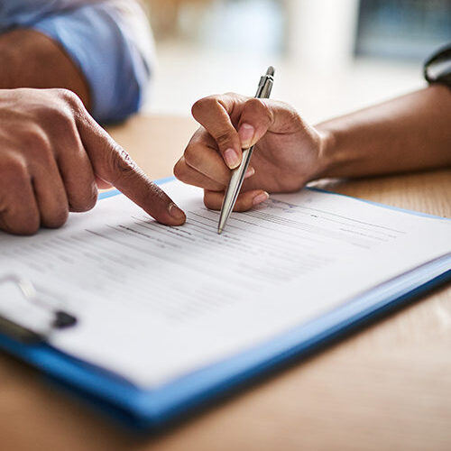 Decorative Image - "Close-up of two people reviewing a document, with one person pointing and the other holding a pen, preparing to sign or fill out paperwork."