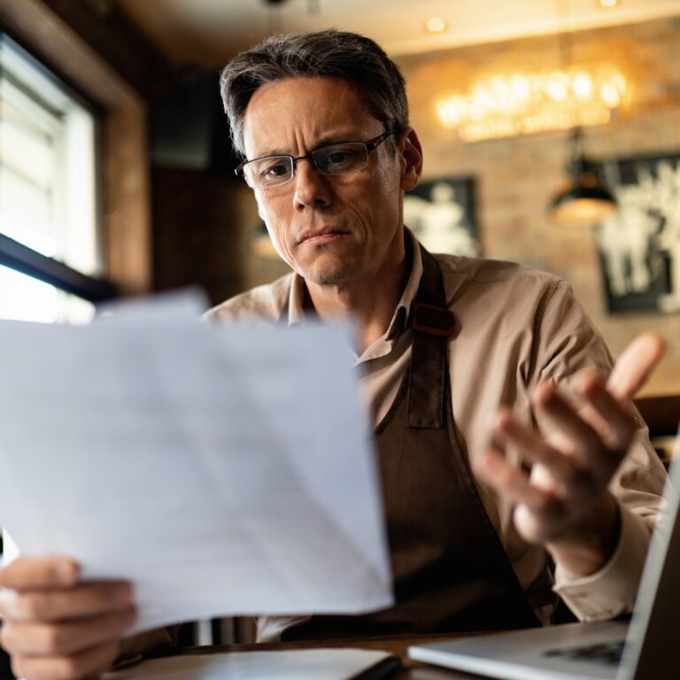 Image: adult business owner feeling confused while reading documents at their computer.