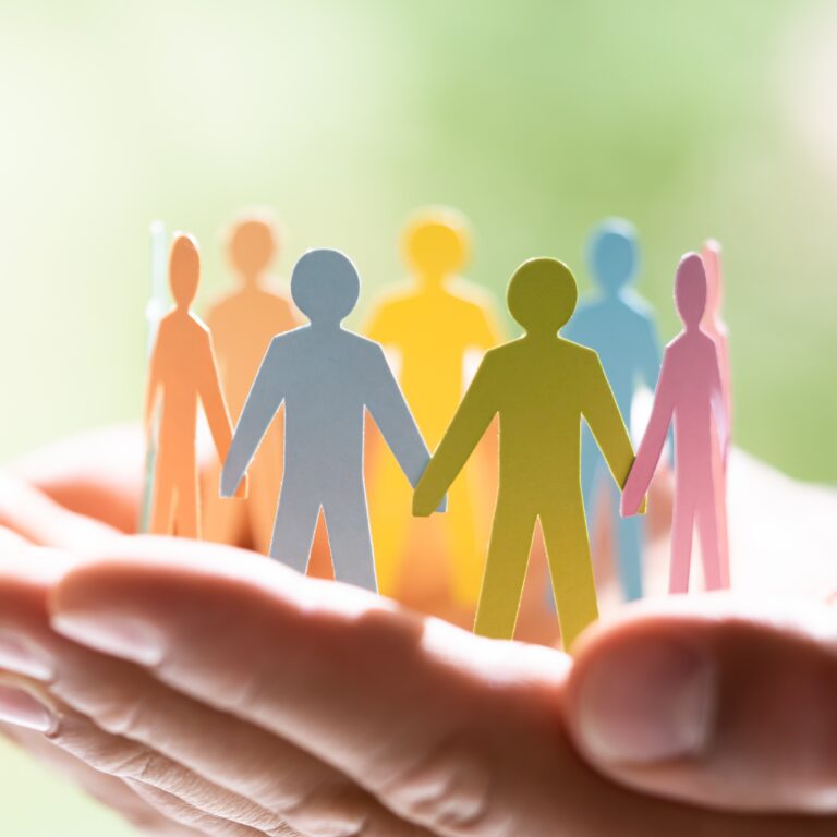 Decorative Image: Close-up of hands gently holding a circle of colorful paper cut-out figures, symbolizing community, diversity, and inclusion.